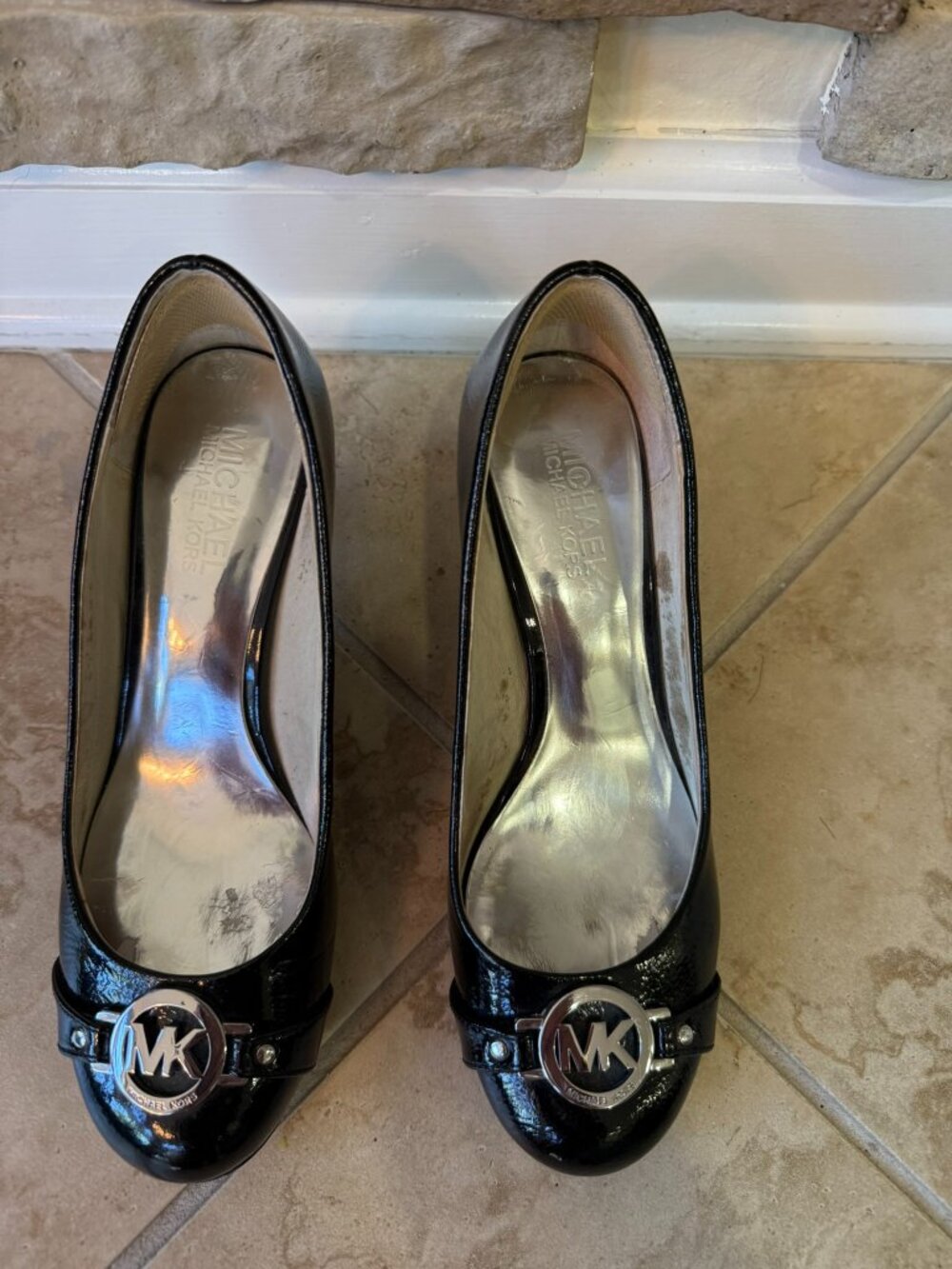 These are Michael Kors black patent leather pumps featuring a silver logo buckle
